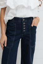 Person wearing dark blue jeans with button details against a white background