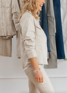 Woman wearing a beige jacket and pants standing in front of a rack of clothing.